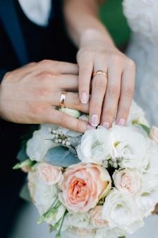 Symbolbild Heirat Zwei Hände mit jeweils einem Ehering, Blumenstrauß